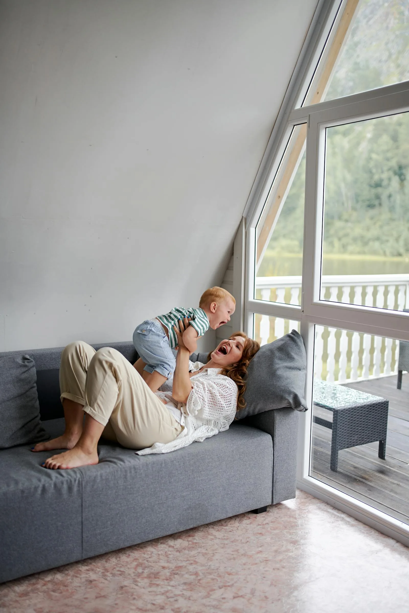 Mutter und Baby spielen lachend in einem hellen Wohnzimmer am grossen Fenster