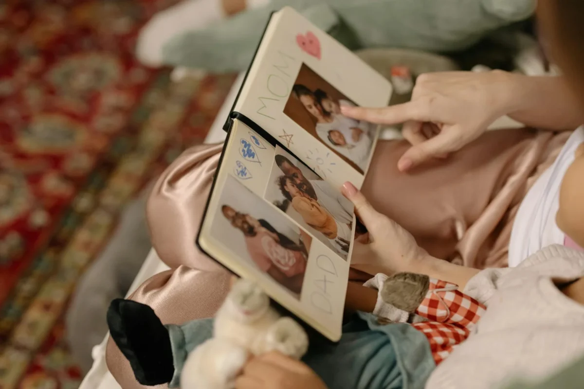 Kind und Erwachsener betrachten gemeinsam ein Familien-Fotoalbum auf dem Sofa